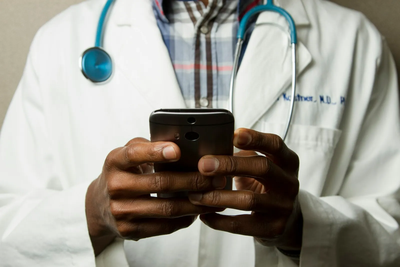 Médico con estetoscopio al cuello usando el teléfono celular